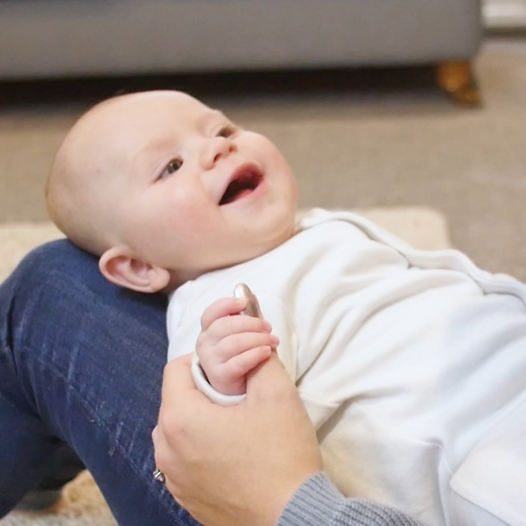 Smiling baby having nails filed with a white Thumble on a parent’s thumb, by Thumble Baby Care.